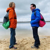 Two people with their Swim Feral Terrapin bags on their backs, next to the water.