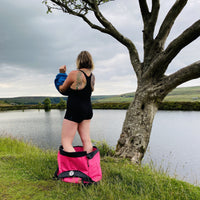 Woman standing in her pink Terrapin Swim Feral bag, getting changed, looking out across the water.
