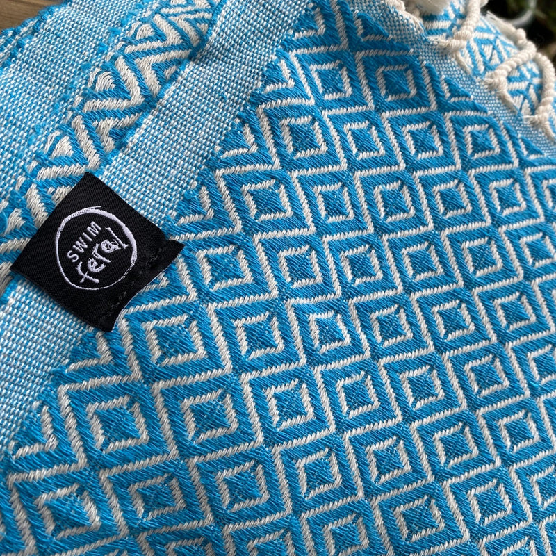 Swim Feral Turkish Towel close up with label showing. Colour: Sky Blue
