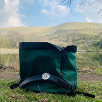 Green Terrapin outdoor swimming bag on the ground with water in the background and hills in the distance. It is a sunny day.