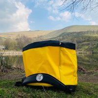 Yellow Terrapin outdoor swimming bag on the ground with water in the background and hills in the distance. It is a sunny day.