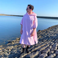 Man standing at the water's edge wearing a Swim Feral organic towelling poncho looking out to the horizon