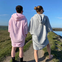 Two people with their backs to the camera wearing Swim Feral organic towelling ponchos on a footpath near the water